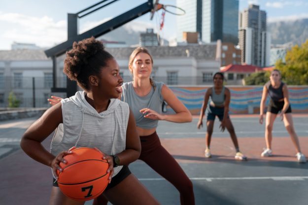 sporten na een blessure vrouw die een blessure heeft gehad heeft een basketbal in haar handen en speelt basketbal met andere vrouwen.