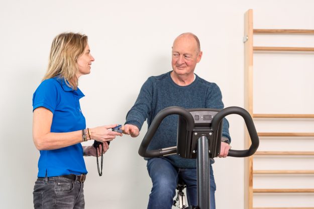 fit uw pensioen in Man in zijn pensioen traint op een hometrainer onder begeleiding van een fysiotherapeut.