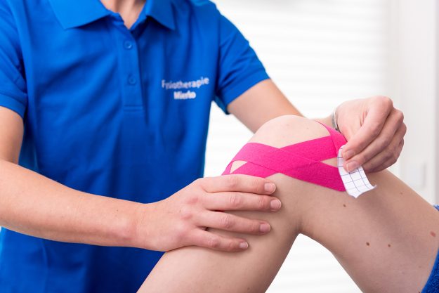 Knakkende knieën fysiotherapeut behandelt patient tegen knakkende knieen door middel van het aanbrengen van roze medical taping