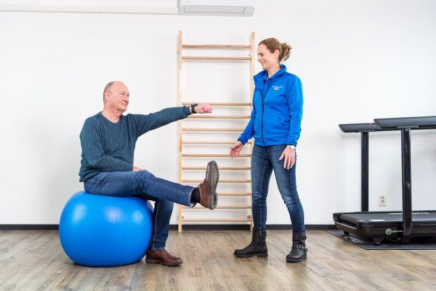 bewegen bij parkinson Man doet aan bewegen bij parkinson in de oefenzaal samen met de fysiotherapeut in een blauw jasje
