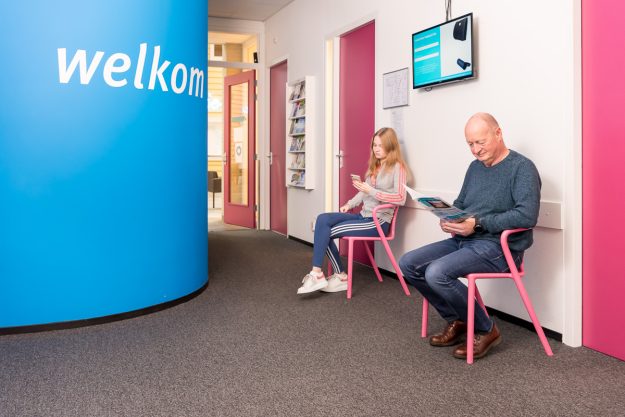 Polsklachten door smartphonegebruik Twee mensen die wachten op hun beurt, maar polsklachten krijgen door smartphone gebruik ondertussen.