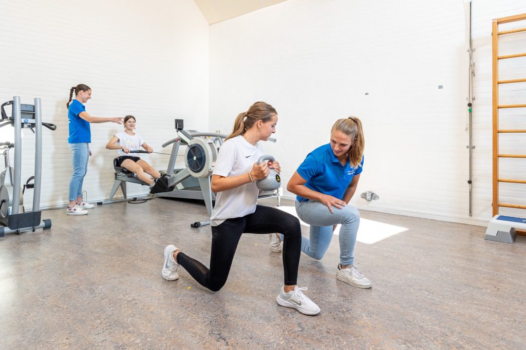Sportieve vrouw die een kettlebell vasthoudt voorkom shin splints in een wit shirt en zwarte sportbroek werkt met behulp van de fysiotherapeut in een blauw shirt
