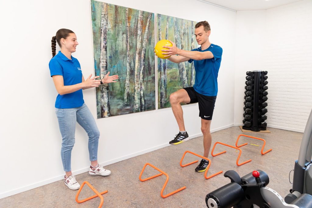 Fysiotherapeut helpt man in blauw shirt met bewegen, zodat hij niet te hard van start gaat met sporten.